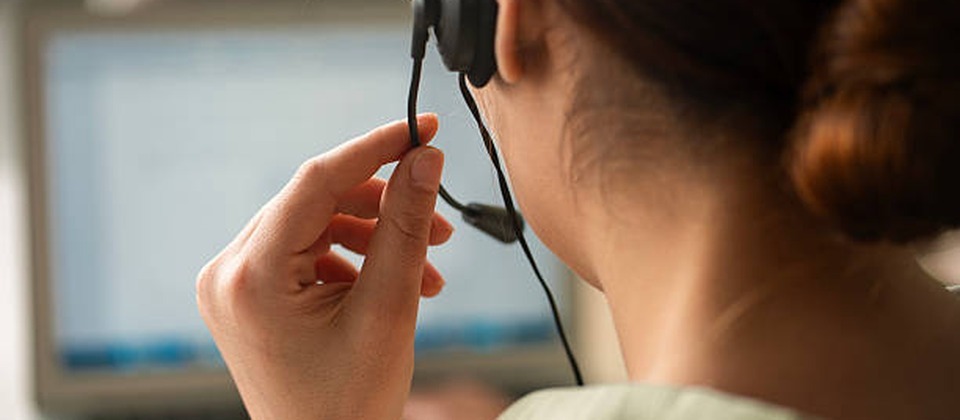 Rear view of a customer support agent adjusting their headset while working on a computer.