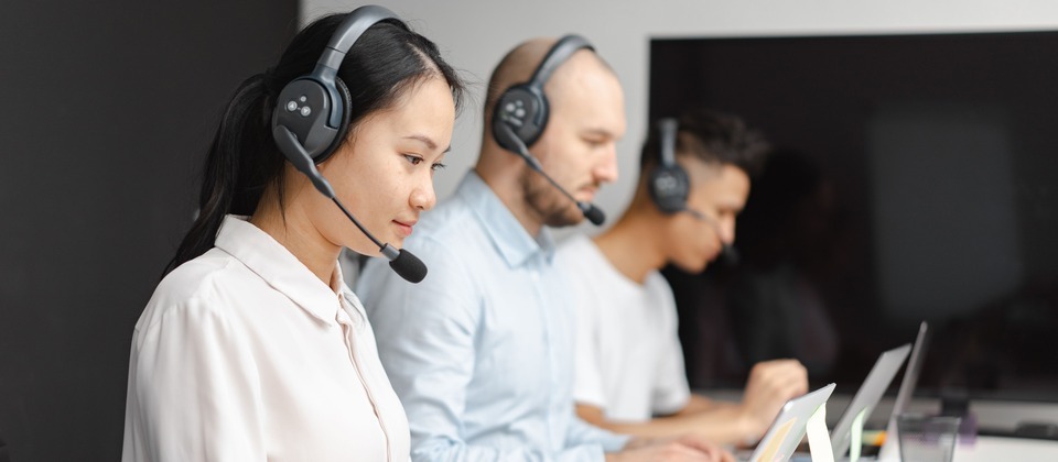 A diverse team of customer support agents wearing headsets and working on laptops in an office.