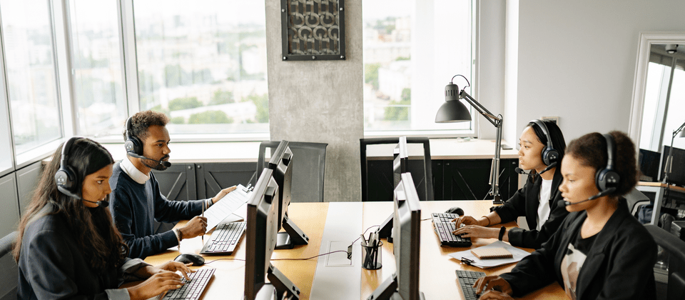 A diverse team of customer support representatives wearing headsets while working on computers in a modern office.