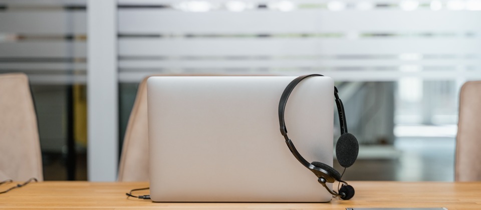 A laptop computer with a call center headset resting on it sitting on a wooden desk in an office.