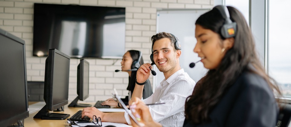 A smiling customer support representative wearing a headset at a desk in a modern office