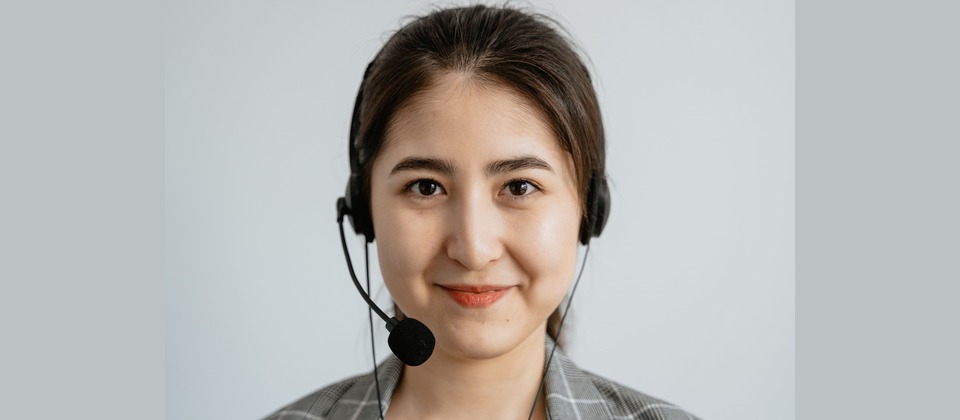 A smiling customer support agent wearing a headset and blazer against a neutral background.